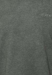 Dunkelgrünes T-Shirt mit kurzen Ärmeln aus weichem, leichtem Stoff; hat eine subtile Textur und ein kleines besticktes Logo.