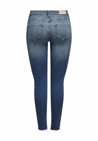 Jeans ajustados de color azul con un lavado desgastado, dos bolsillos traseros y un dobladillo deshilachado. Hechos de un material de mezclilla con una textura suave.