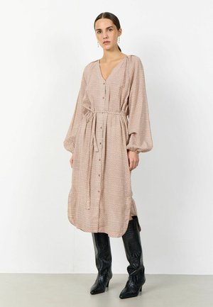 Mujer de pie vistiendo un vestido midi de manga larga abotonado con cinturón y botas negras altas con textura hasta la rodilla.