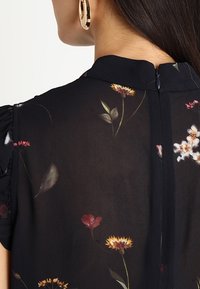 Black sheer blouse featuring a floral pattern, puffed short sleeves, and a back closure with a small zipper.