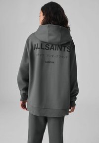 Felpa grigia con cappuccio che presenta un grande testo nero "ALLSAINTS" sul retro, tessuto morbido, vestibilità comoda e polsini e orlo a coste.