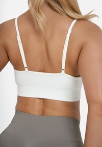 Bela ribasta braletka z nastavljivimi naramnicami in prilegajočim se dizajnom. Tkanina je gladka z rahlim raztezanjem, primerna za udobje in podporo.