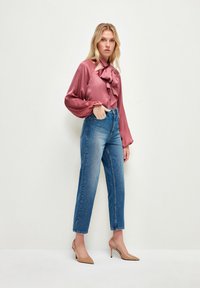 Blusa de satén rosa con un lazo y volantes, combinada con jeans de mezclilla azul claro de tiro alto y zapatos de tacón beige.