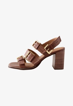 Sandale à talon en cuir marron avec trois brides à boucle dorée réglables et un talon bloc en bois sur fond blanc.
