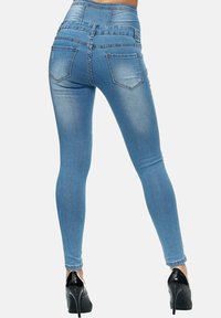Jeans skinny de mezclilla azul de cintura alta con una textura suave, presentan dos bolsillos traseros y piernas ajustadas, combinados con tacones altos negros.
