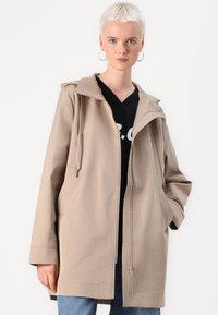 Casaco bege com capuz, fabricado em tecido suave, com fecho éclair, dois bolsos laterais e cordões no capuz para ajustabilidade.