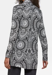 Svart och vit långärmad skjorta med intrikata cirkulära mönster, mandalas och paisleymotiv på ett mjukt tyg.