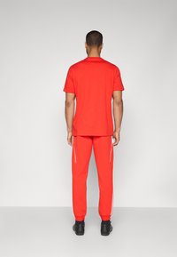 Rød kortermet t-skjorte og røde joggebukser med hvite side Striper, laget av glatt stoff, med avslappet passform og elastiske mansjetter.