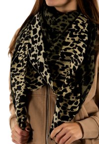 Foulard en imprimé léopard noir et beige, grand et doux, avec des bords frangés. Porté lâchement sur une veste beige zippée, mettant en valeur son design texturé.