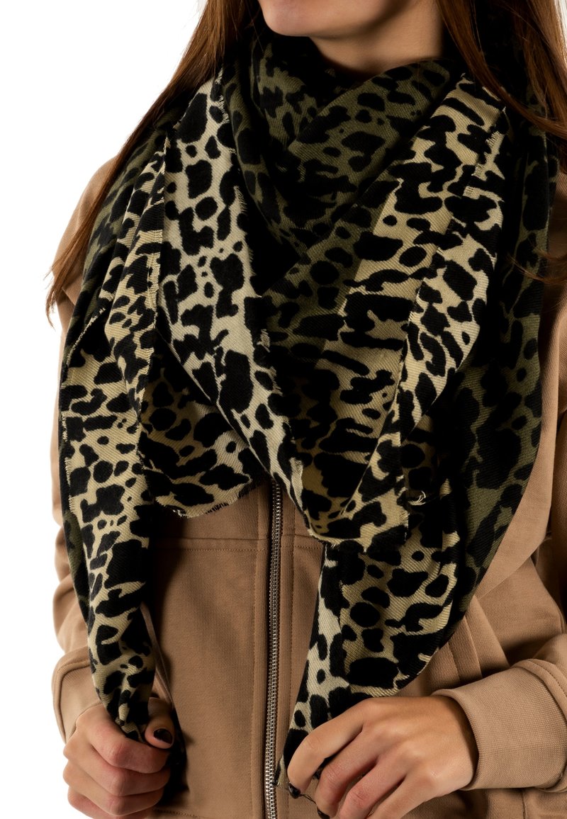 Foulard en imprimé léopard noir et beige, grand et doux, avec des bords frangés. Porté lâchement sur une veste beige zippée, mettant en valeur son design texturé.