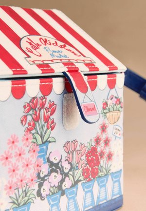 Mała torebka z czerwono-białym paskowanym wierzchem, niebieską r ączką i ilustrowanymi kwiatami w niebieskich doniczkach na jasnoniebieskim tle.