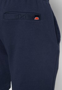 Marineblaue Sweatshorts aus glattem Baumwollstoff, mit einer Gesäßtasche und einem rot-weißen Logostick. Einfaches, entspanntes Design.