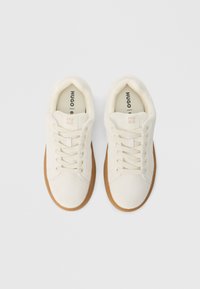 Fehér vászon tornacipő texturált felsőrésszel, kerek orrú, bézs színű fűzőkkel és világosbarna gumitalppal. A logó a nyelvén nyomtatott.