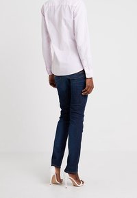 Jeans di denim blu scuro abbinati a una camicia button-up a righe rosa chiaro. La camicia presenta polsini con bottone e un colletto classico.