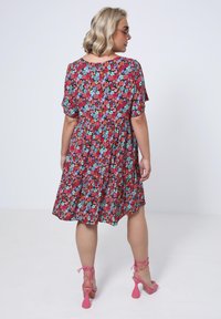 Floral dress with short sleeves, red background, and multicolored flowers. Knee-length, flared design, paired with pink strappy heels.