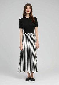 Haut noir à rayures avec manches courtes associé à une longue jupe rayée noir et blanc. Chaussures noires à enfiler. Tissu lisse avec un design fluide.