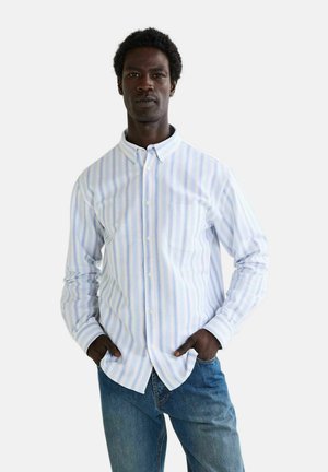 Chemise à boutons en bleu clair avec des rayures verticales dans des coloris pastel. Comprend une poche poitrine et un col classique. Associée à un jean en denim.