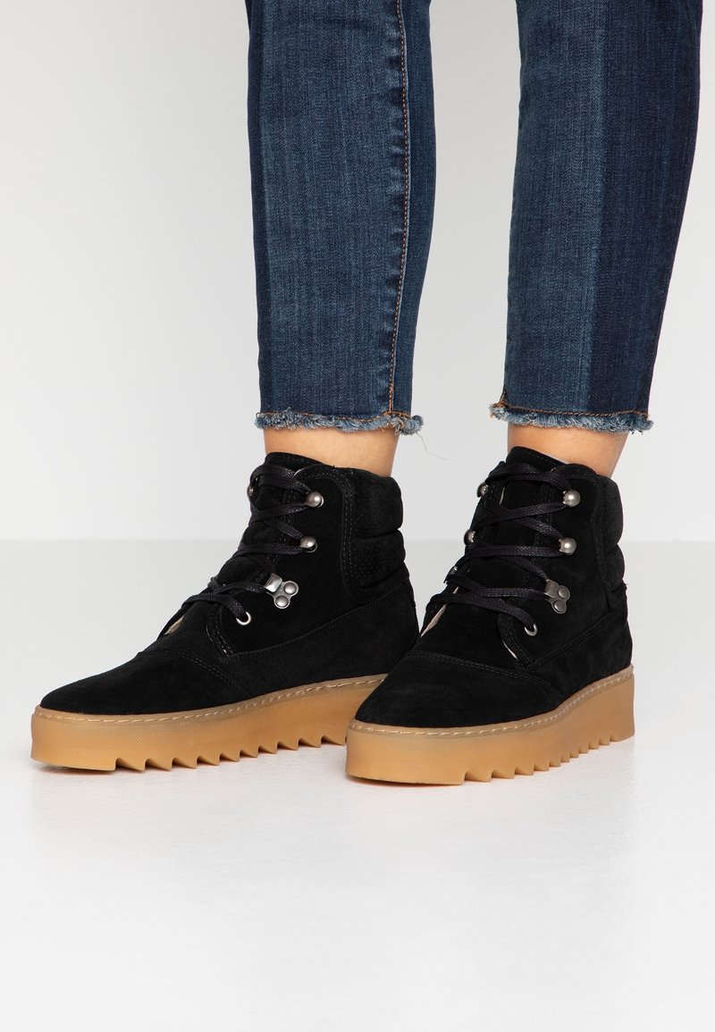 Stivali alla caviglia in suede nero con una parte superiore texturizzata e una suola in gomma spessa. Presentano occhielli in metallo e lacci per una chiusura sicura.