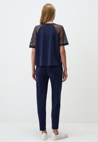 Completo blu navy con una maglia svolazzante e maniche in rete e pantaloni aderenti. Il materiale sembra morbido, con una texture liscia e una leggera lucentezza.