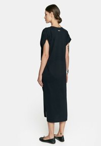Czarna sukienka z długim rękawem, wykonana z lekkiego materiału. Posiada boczne rozcięcia, luźny krój oraz subtelny detal z tyłu. Noszona z czarnymi balerinkami.