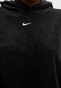 Černá kordurová mikina s kapucí s vroubkovanou texturou a bílým logem Nike na hrudi. Navržena s uvolněným střihem a kapucí.