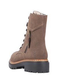 Brązowy zamszowy botek za kostkę z wyściełanym kołnierzem, sznurowanym przodem, bocznym zamkiem błyskawicznym, kontrastującymi jasnobrązowymi przeszyciami i masywną czarną gumową podeszwą.
