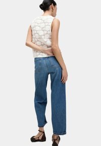Weißes gehäkeltes Tanktop mit strukturiertem Muster, kombiniert mit lockeren blauen Denim-Jeans mit geradem Bein und aufgerollten Säumen. Braune Riemchenschuhe.