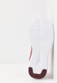 Bordó teniska s texturovaným síťovaným svrškem a bílou gumovou podrážkou. Má drážkovaný vzor pro lepší přilnavost a logo Reebok na podrážce.