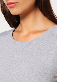 Haut gris avec un col rond, texture douce et motif léger en côtes. La vue en gros plan se concentre sur la zone des épaules et du cou.