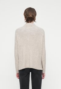 Beige stickad tröja med avslappnad passform, som har hög krage, sänkta axlar och en något längre bakre fåll. Mjuk textur.