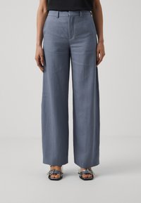Pantaloni blu chiaro a gamba larga con una texture liscia, vita media e pieghe nette; abbinati a sandali neri con hardware argentato.