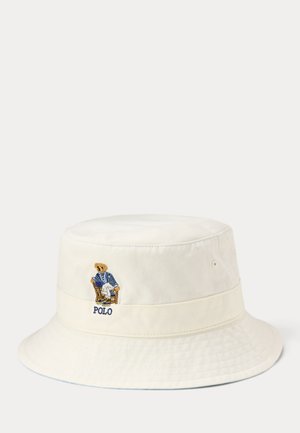 Off-white bucket hat met geborduurde beer die een blauwe blazer draagt en op een stoel zit, met de tekst "POLO" onder de beer.