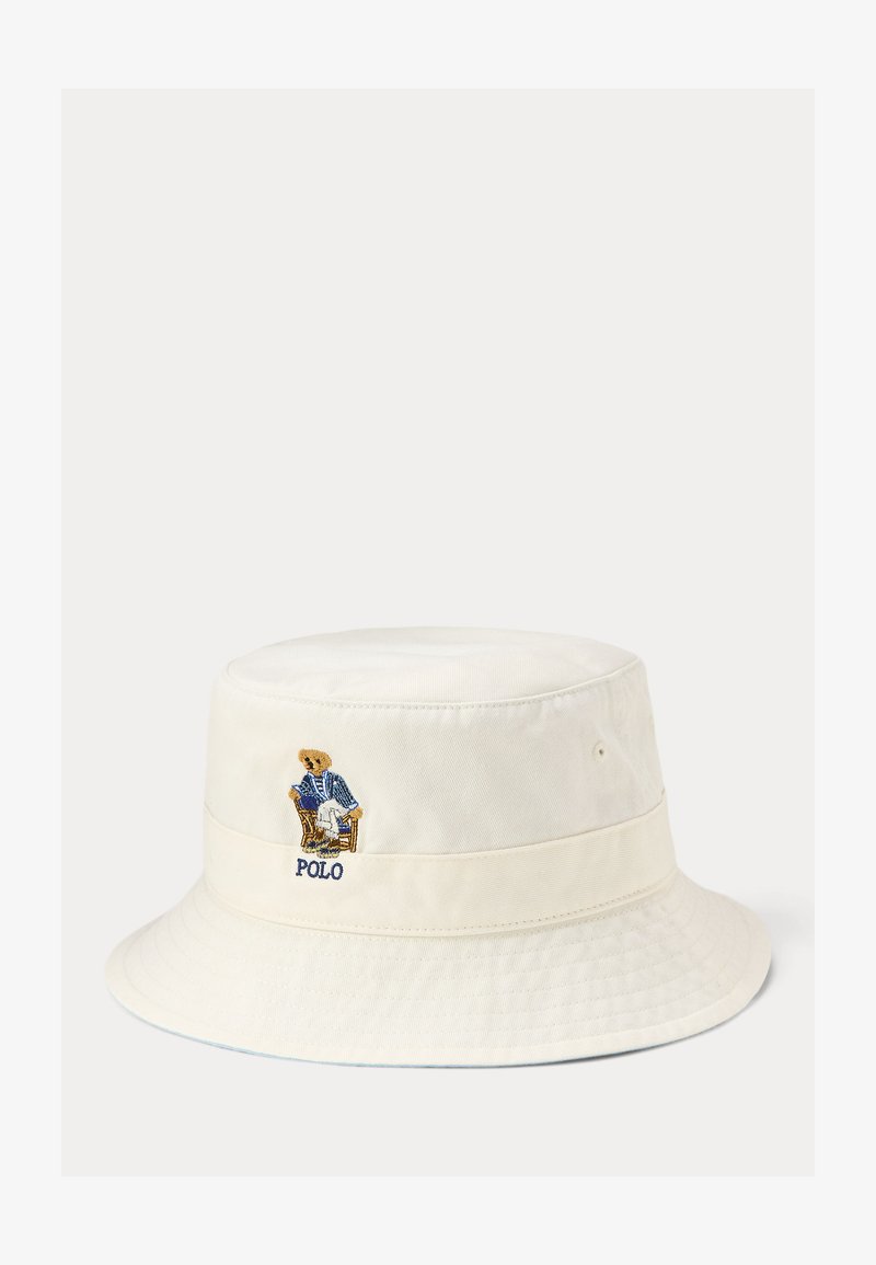 Chapeau bob blanc cassé avec un ours brodé portant un blazer bleu assis sur une chaise, avec le texte « POLO » en dessous de l'ours.