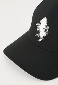 Cappellino da baseball nero realizzato in un tessuto testurizzato, con un logo di cavallo bianco ricamato in evidenza sulla parte frontale.