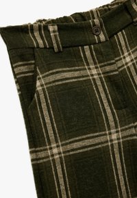 Zielone spodnie w kratę wykonane z miękkiego materiału, z zapięciem na guzik, elastycznym pasem i skośnymi kieszeniami po bokach.