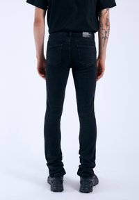 Jeans ajustados negros de mezclilla, con una cintura de altura media, diseño de cinco bolsillos y detalles de costura mínimos.