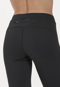 Svarta träningsleggings i stretchigt material, med platta sömmar, en bakficka och en slät yta utan mönster.