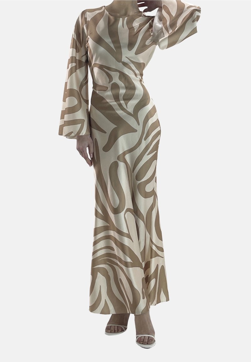 Longue robe beige et blanche à motif abstrait, manches longues et taille cintrée, portée avec des talons blancs ouverts à l'avant.