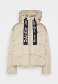 Beige pufferjakke med hætte; har lodret quiltning, lynlsluk og sorte mærke-drawstrings på halsen. Glat, skinnende tekstur.