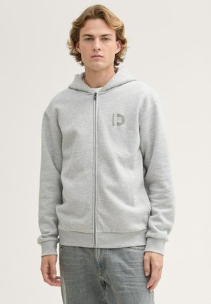 Grau Zip-Hoodie mit Kordelzugkapuze, auf der linken Brust mit einem kleinen Logo in gedämpften Tönen. Weicher, strukturierter Stoff. Lässige Passform.
