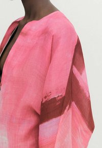 Kaftan léger présentant des motifs en coups de pinceau rose et rouge profond, avec une coupe ample et un décolleté en V, confectionné dans un tissu texturé.