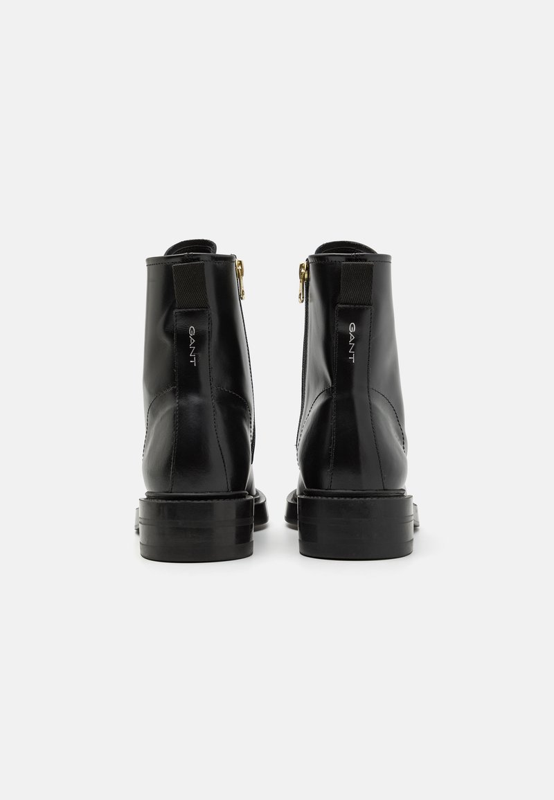 Bottes noires en cuir à hauteur de cheville avec une finition lisse, des zips sur le côté et un détail de logo sur le talon. Semelle épaisse avec un léger brillant.