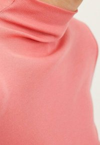 Pull à col roulé rose en tissu doux et élastique, au design ajusté et à la texture lisse, montrant un gros plan du décolleté.