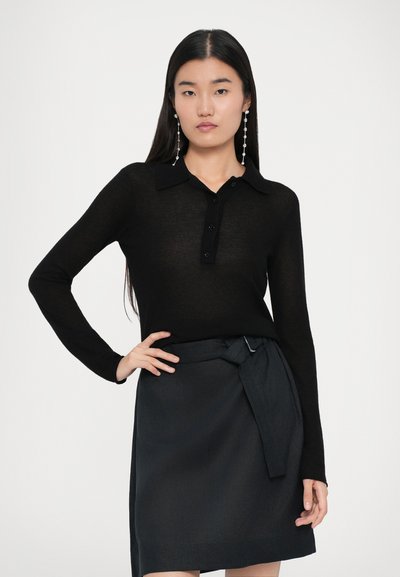 Svart långärmad polo med knäppning och krage, matchad med en mörk kjol med en knytning i midjan.