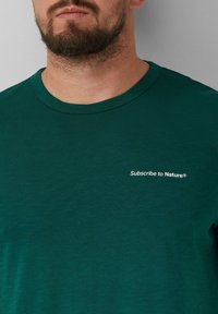 Groene T-shirt met korte mouwen van zachte stof, met een ronde halslijn en een witte geborduurde logo: "Abonneer je op de Natuur®."