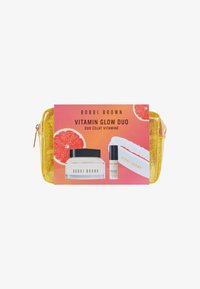 Bobbi Brown Vitamin Glow Duo Set mit einem gelben Glitzeretui, einem weißen Haarband, einem Glas mit Creme und einem Serum in einem klaren Behälter.