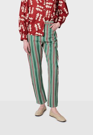 Rood gebloemd overhemd met knopen, gecombineerd met groen en wit gestreepte broek. De broek heeft een rechte pijpdesign; de schoenen zijn beige met uitsparingen.