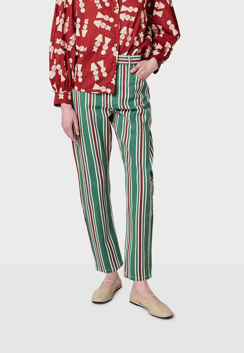 Červená košeľa s vzorom a gombíkmi, kombinovaná so zelenými a bielymi pruhovanými nohavicami. Nohavice majú strih rovného strihu; topánky sú béžové s výrezmi.