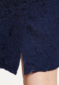 Námorní krajková látka s květinovými vzory, s volánovým lemem a bočním rozparkem pro zvýšení textury a designu.