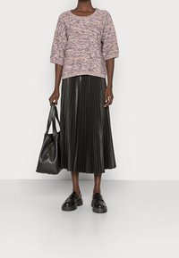 Pull en maille violet à pois avec des manches courtes, associé à une jupe en cuir plissée noire. Sac à épaule en cuir noir et chaussures noires massives.